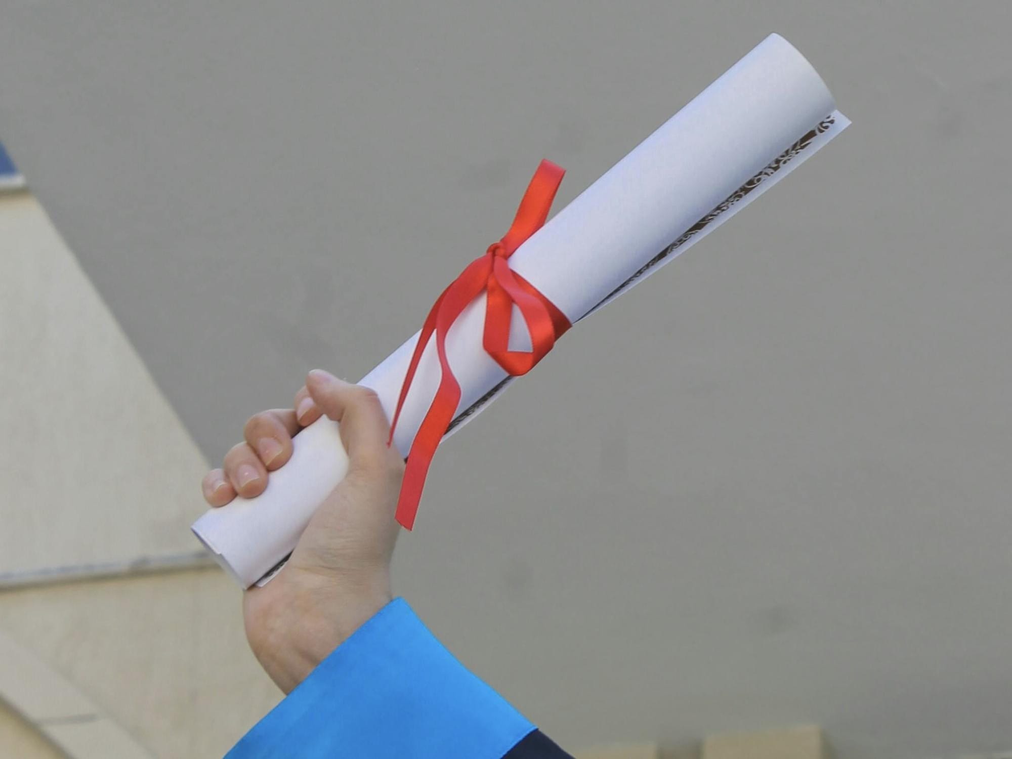 Photograph of a hand holding a rolled up degree tied with a red ribbon.